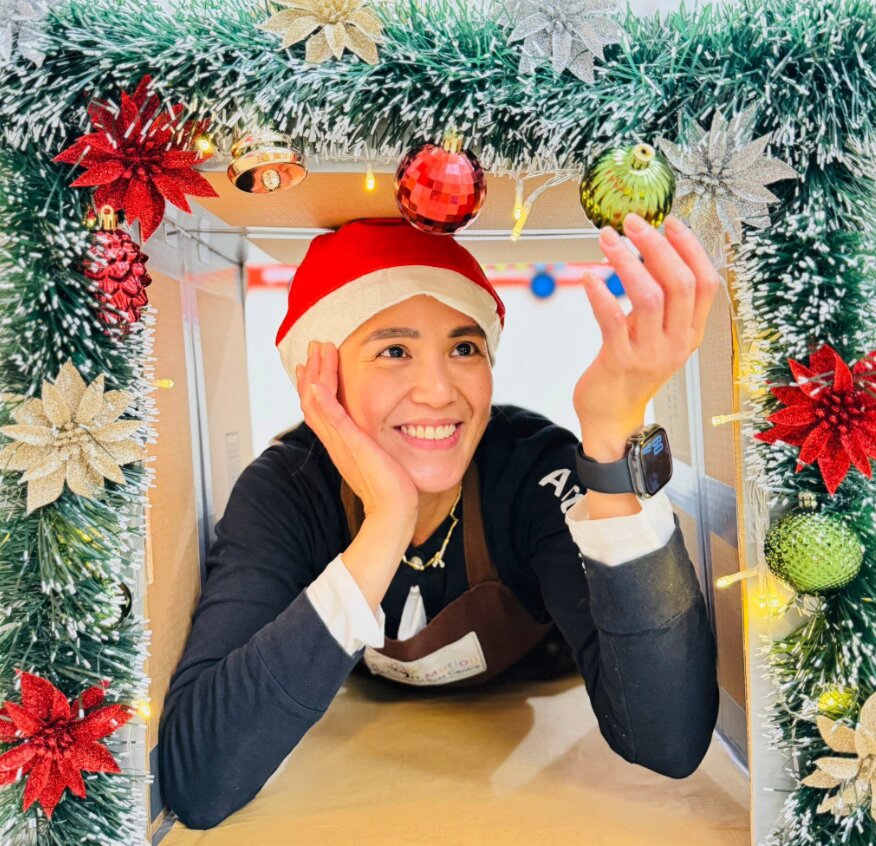 Jowena smiling inside a handmade holiday photobooth decorated with tinsel and ornaments