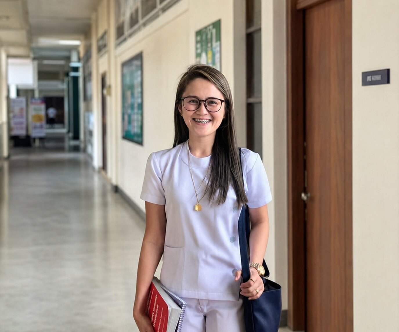 Jowena in scrubs holding textbooks in a hospital hallway during her midwifery studies