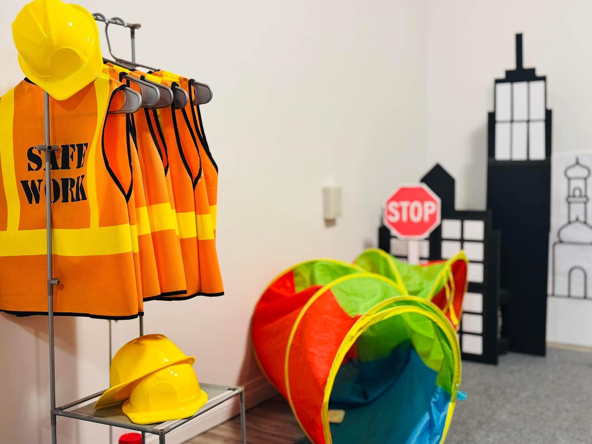 Safety vests, hard hats, and a play tunnel with a cardboard city skyline in the background
